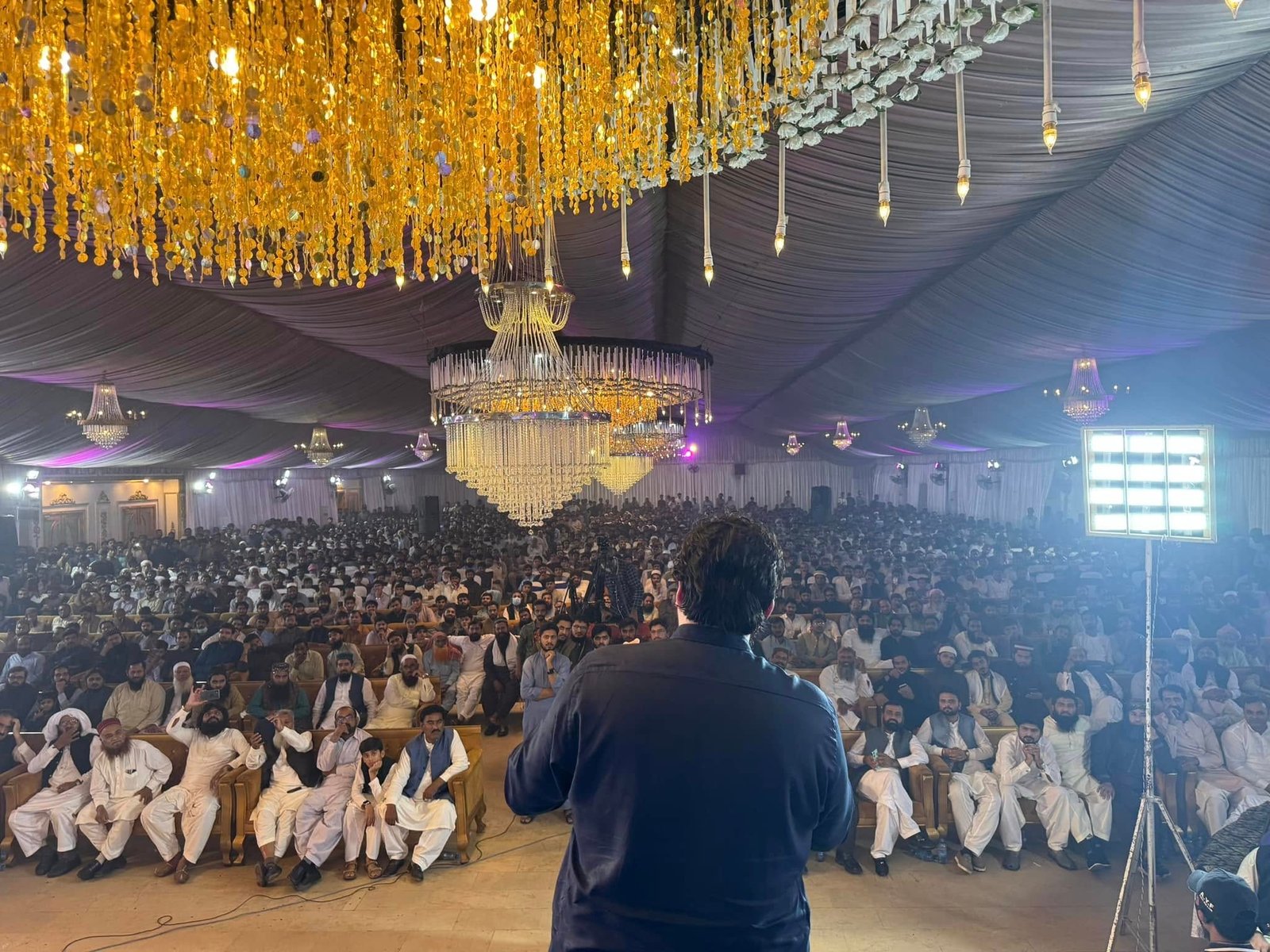 Wide view of the event hall with decorative chandeliers and seated audience