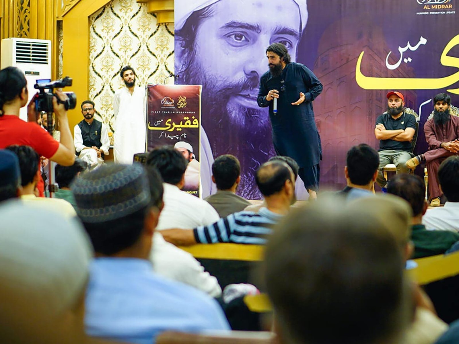 Main speaker delivering speech in front of large backdrop poster