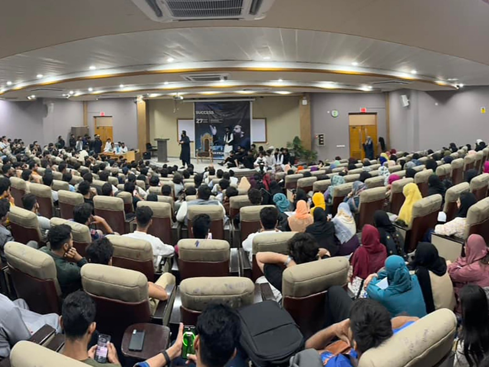 Rear angle showing seated audience and stage setup at Lahore youth event