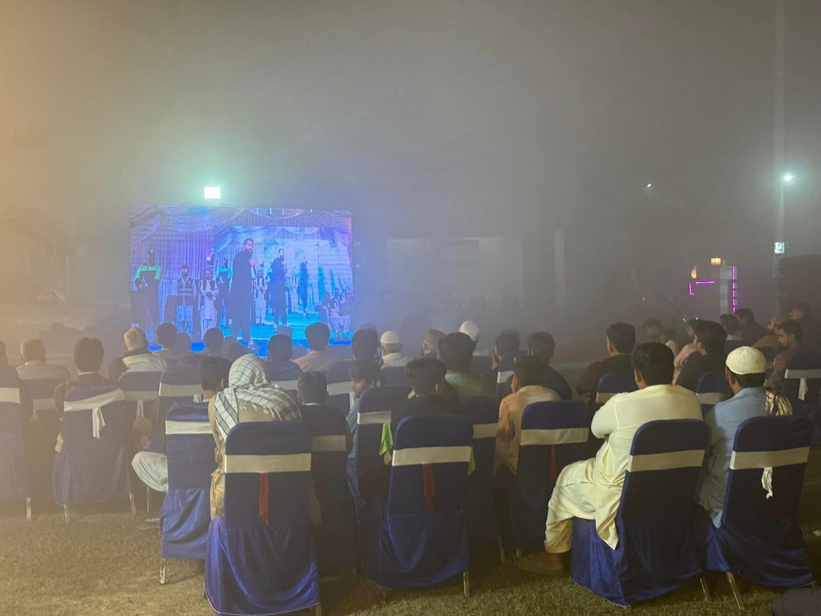 Speaker on stage under grand chandeliers at Mailsi Jalsa main session